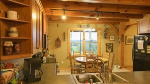 Una cocina con armarios de madera, una cafetera, un fregadero y un comedor con sillas y una mesa.