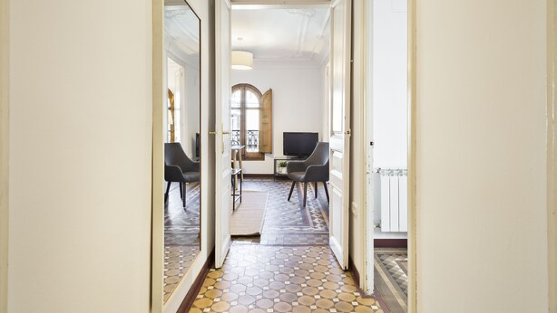 A hallway with a tiled floor, a television on a stand, and two chairs.