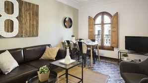 A living room with a sofa, coffee table, TV, and a dining area with chairs and a table.