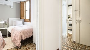 A bedroom with a bed, bedside table, lamp, and a window with an open door leading to a bathroom.