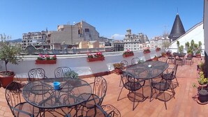 A rooftop terrace with outdoor seating, potted plants, and a view of surrounding buildings.