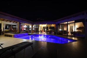 A swimming pool with a blue-lit edge, surrounded by a covered patio area with seating and a view of the interior. - Spectacular Luxury Vacation Home - Breathtaking Views - Best Climate (Atenas)