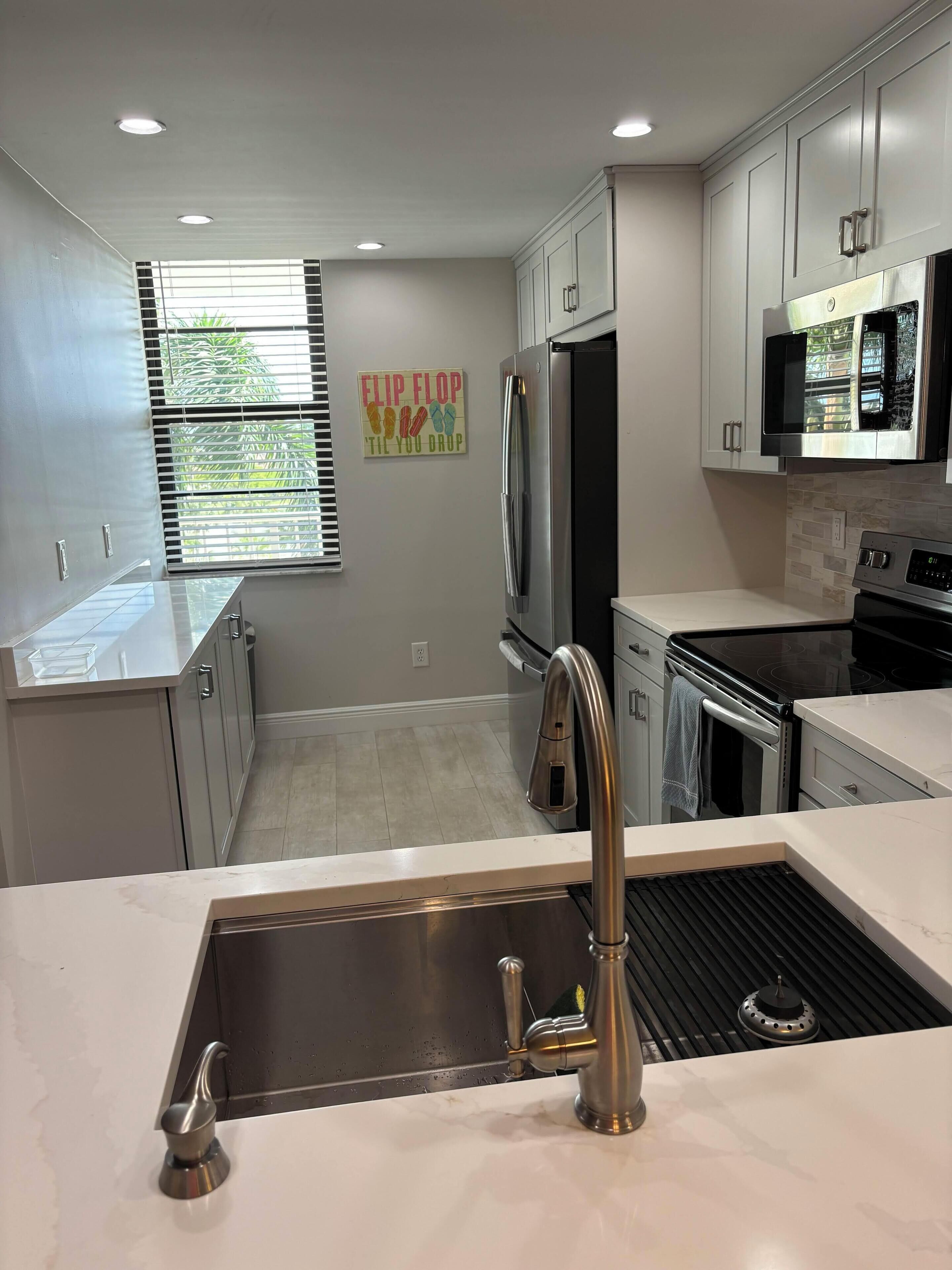A modern kitchen with stainless steel appliances, a sink with a single faucet, and a window with blinds.