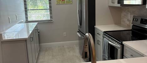 A modern kitchen with stainless steel appliances, a sink with a single faucet, and a window with blinds.