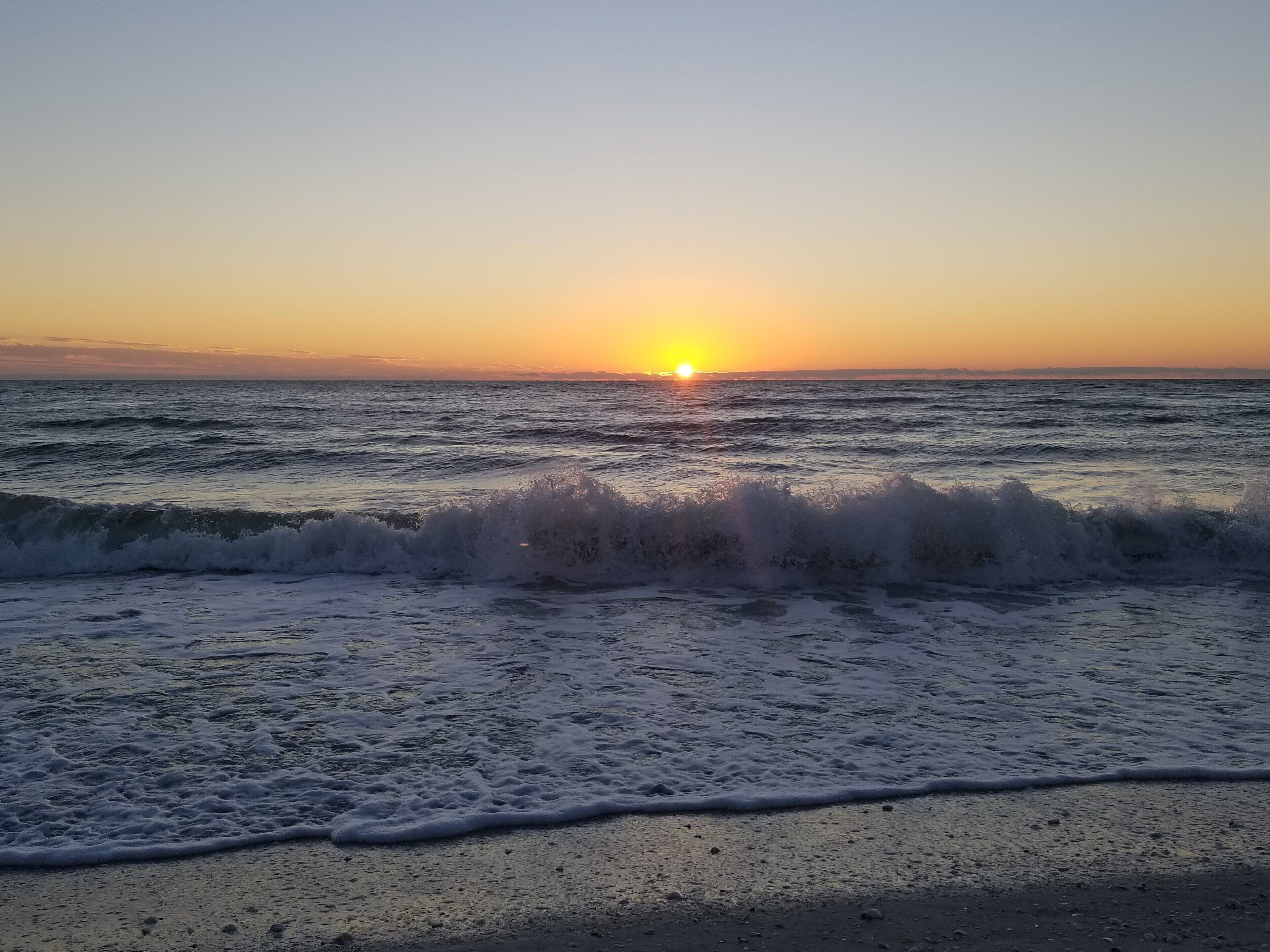 A beach with waves and a sunset in the background.