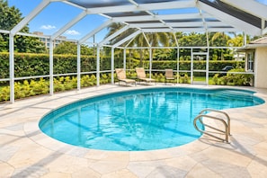 A covered swimming pool with a curved edge, surrounded by a white pergola, and a tiled patio area with lounge chairs.
