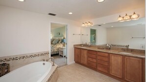 A bathroom with a large bathtub, wooden cabinets, a sink, and a mirror. - 5-Min Walk to Beach! Private Heated Pool & 5BR Home (Marco Island)
