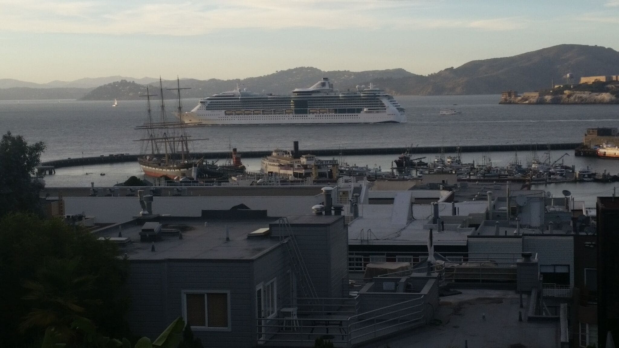 A cruise ship docked at a port with a marina and buildings in the foreground.