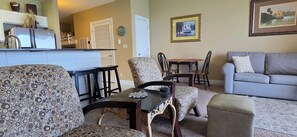 A living room with patterned furniture, a dining area with chairs and a table, and a kitchen area with a refrigerator and cabinets. - {L@@K} Beach FRONT, Home @ the Beach w/Beach Chair Service {L@@K} (Panama City Beach)