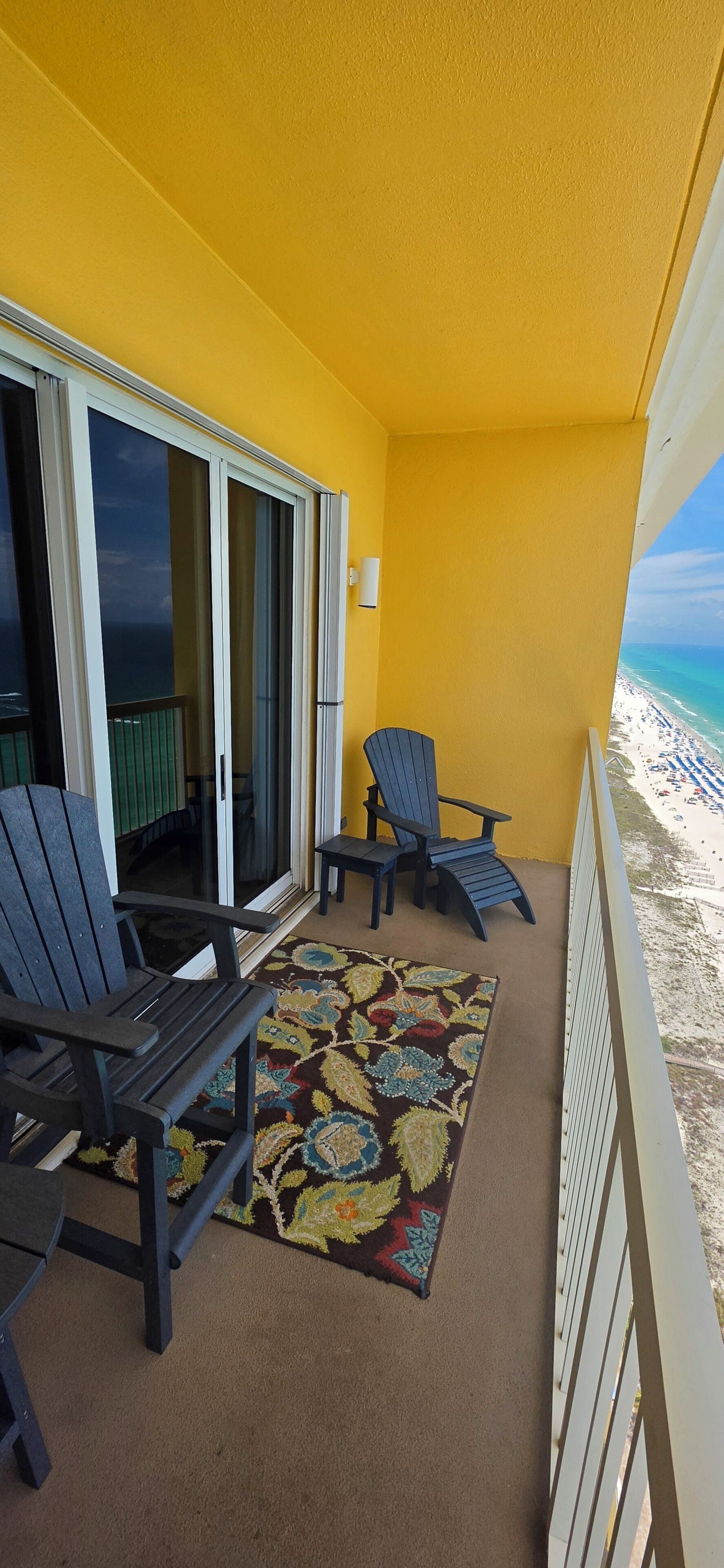 Un balcon avec deux fauteuils Adirondack, un tapis à motifs et une vue sur la plage.