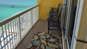 A balcony with a view of the ocean and a pier, featuring a yellow wall, a patterned rug, and several black chairs. - {L@@K}  Beach FRONT, Home @ the Beach w/Beach Chair Service {L@@K} (Panama City Beach)