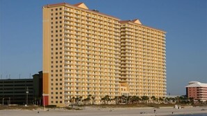 A large, multi-story hotel with a uniform facade, located near a beach with visible palm trees and a sandy shoreline. - {L@@K}  Beach FRONT, Home @ the Beach w/Beach Chair Service {L@@K} (Panama City Beach)