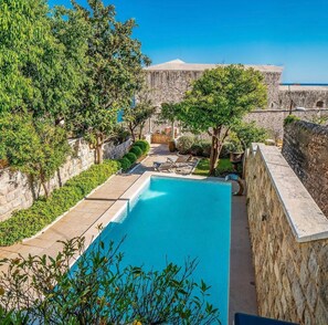 A pool area with a stone wall, trees, and a view of a historic building.