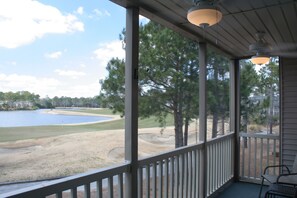 A covered porch with a view of a golf course and a lake.