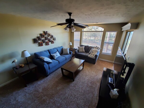 A living room with a blue sofa, a coffee table, a ceiling fan, and a wall decorated with artwork.