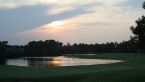 Golfkenttä auringonlaskun aikaan, jossa on vesiesteitä, hiekkabunkkereita ja lippu viheriöllä.