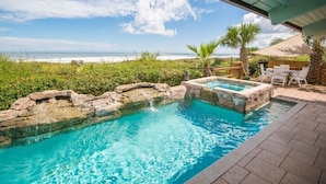 A pool with a view of the beach, surrounded by palm trees and a wooden deck.