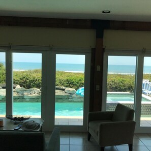 A room with large windows overlooking a pool and ocean view. - Beach Front/heated pool/spa. Ocean Views, Umbrella+Lounger for beach, Balconies (St Augustine)