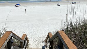 A wooden boardwalk leading to a beach with a clear view of the ocean.