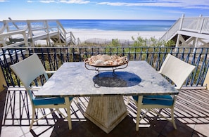 Una mesa con sillas y un cuenco de conchas marinas en un balcón con vista a la playa.