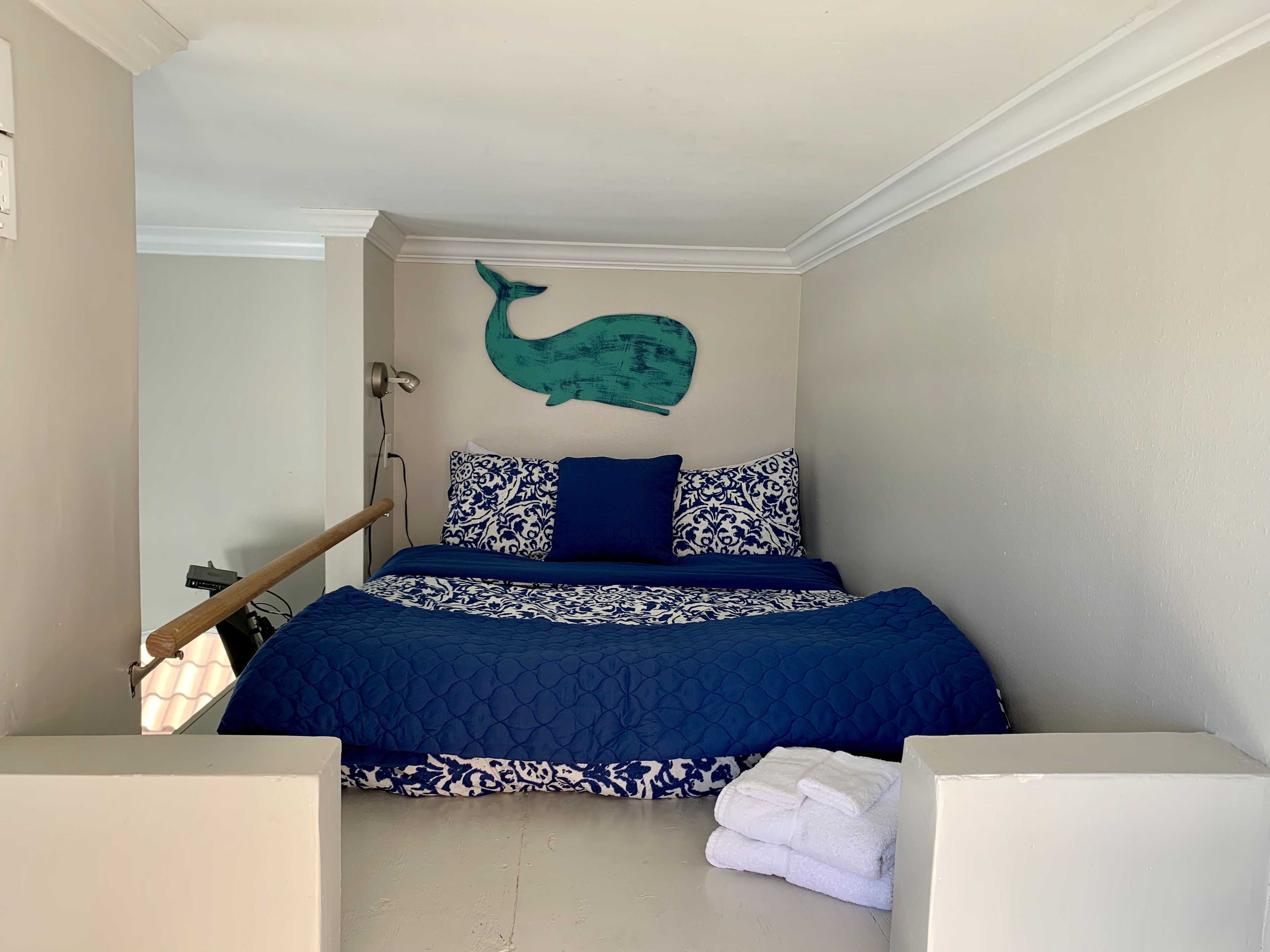 A bedroom with a bed, a wall-mounted whale decoration, patterned pillows, and a stack of white towels.