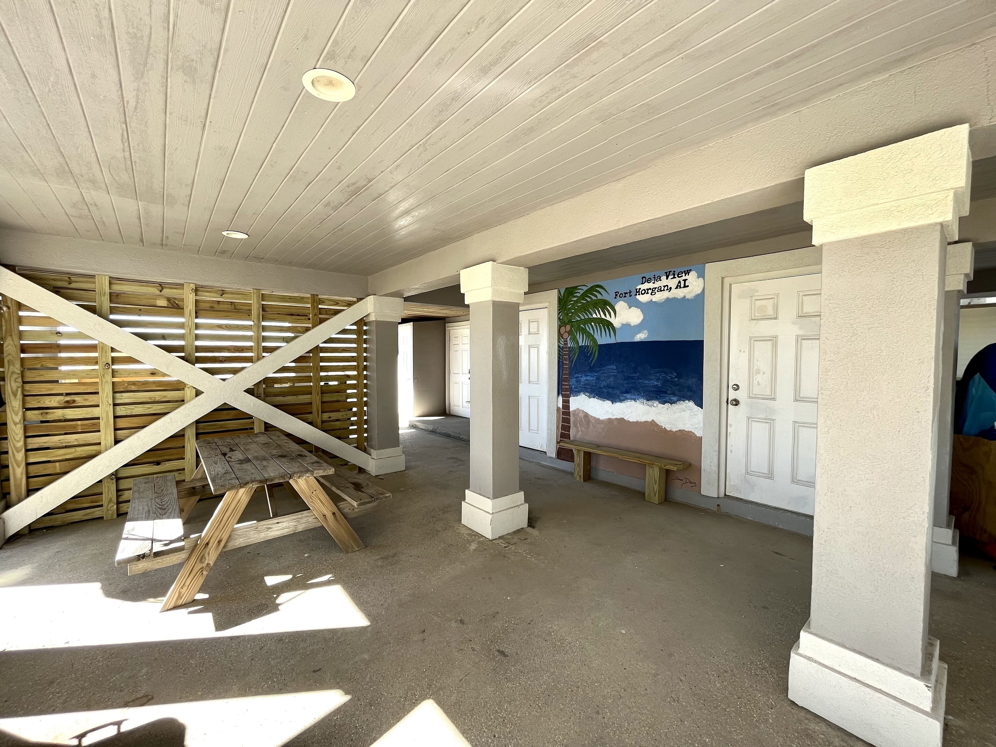 Un couloir avec un mur lambrissé en bois, un banc et une fresque représentant une scène de plage.