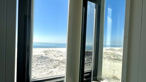Habitación con dos ventanas amplias que dan a una playa y al océano.