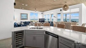 Amplia sala de estar con isla de cocina, ventanas grandes y vista al océano.