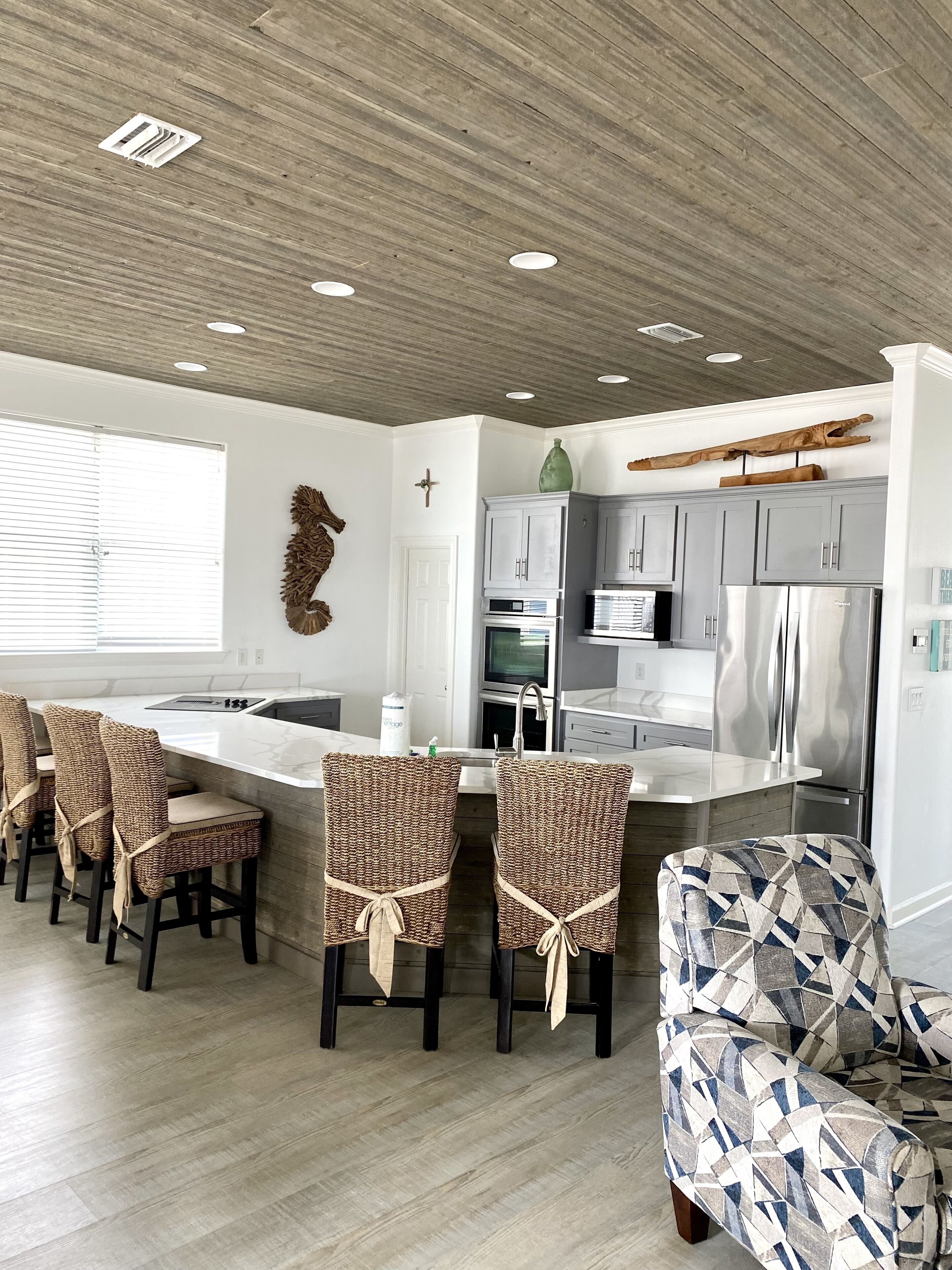 A modern kitchen with a central island, built-in appliances, and a dining area with wicker chairs.