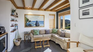 En hyggelig stue med en hjørnesofa, træborde og et maleri af et kystlandskab.