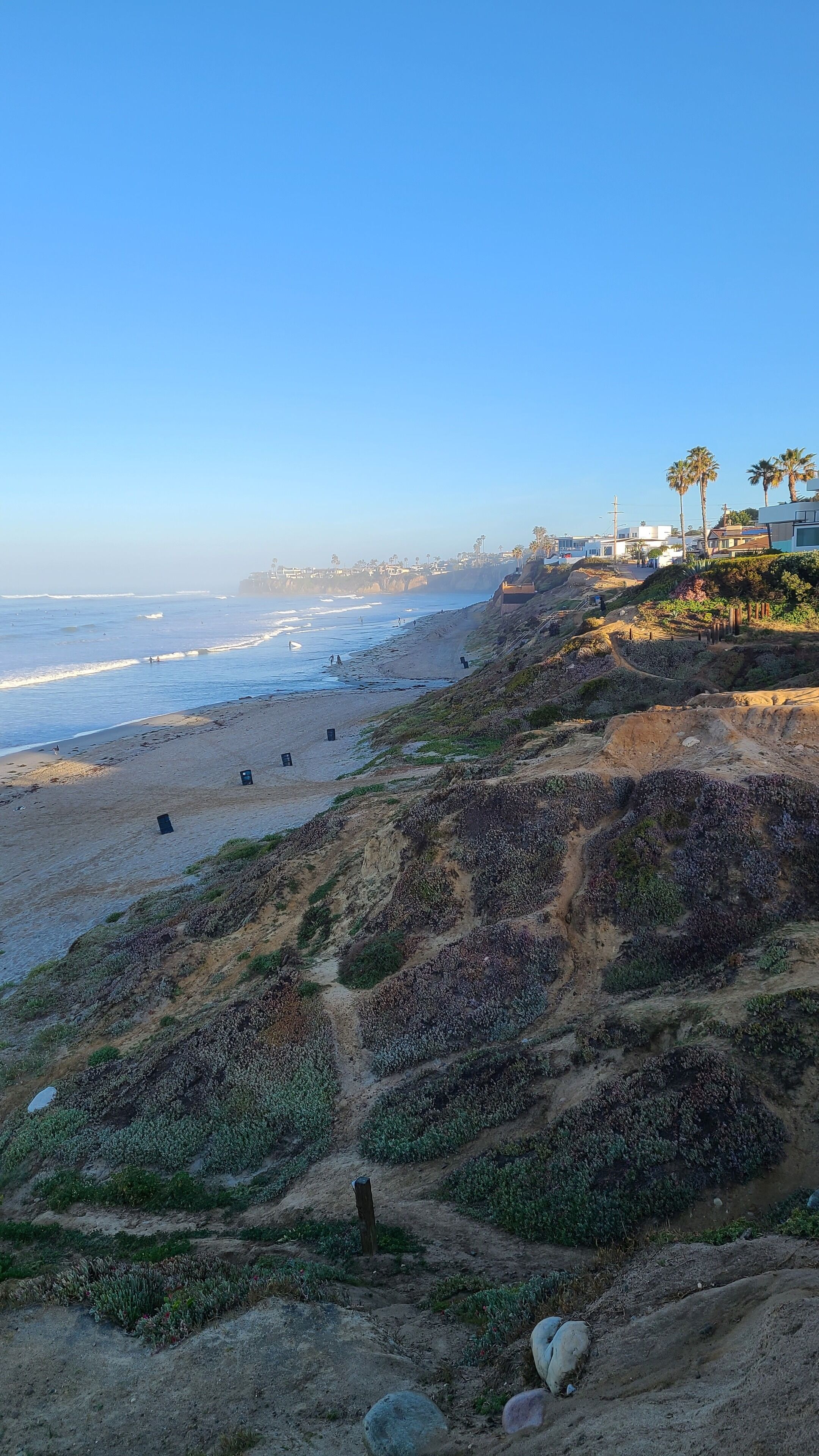 A coastal landscape with a sandy beach, rocky terrain, and a clear blue sky.