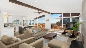 A modern living room with a sofa set, a coffee table, and a fireplace. There is a kitchen area with a dining table and chairs visible through large windows. - Newly Remodeled with VIEWS of Downtown Ocean and Bay! (San Diego)