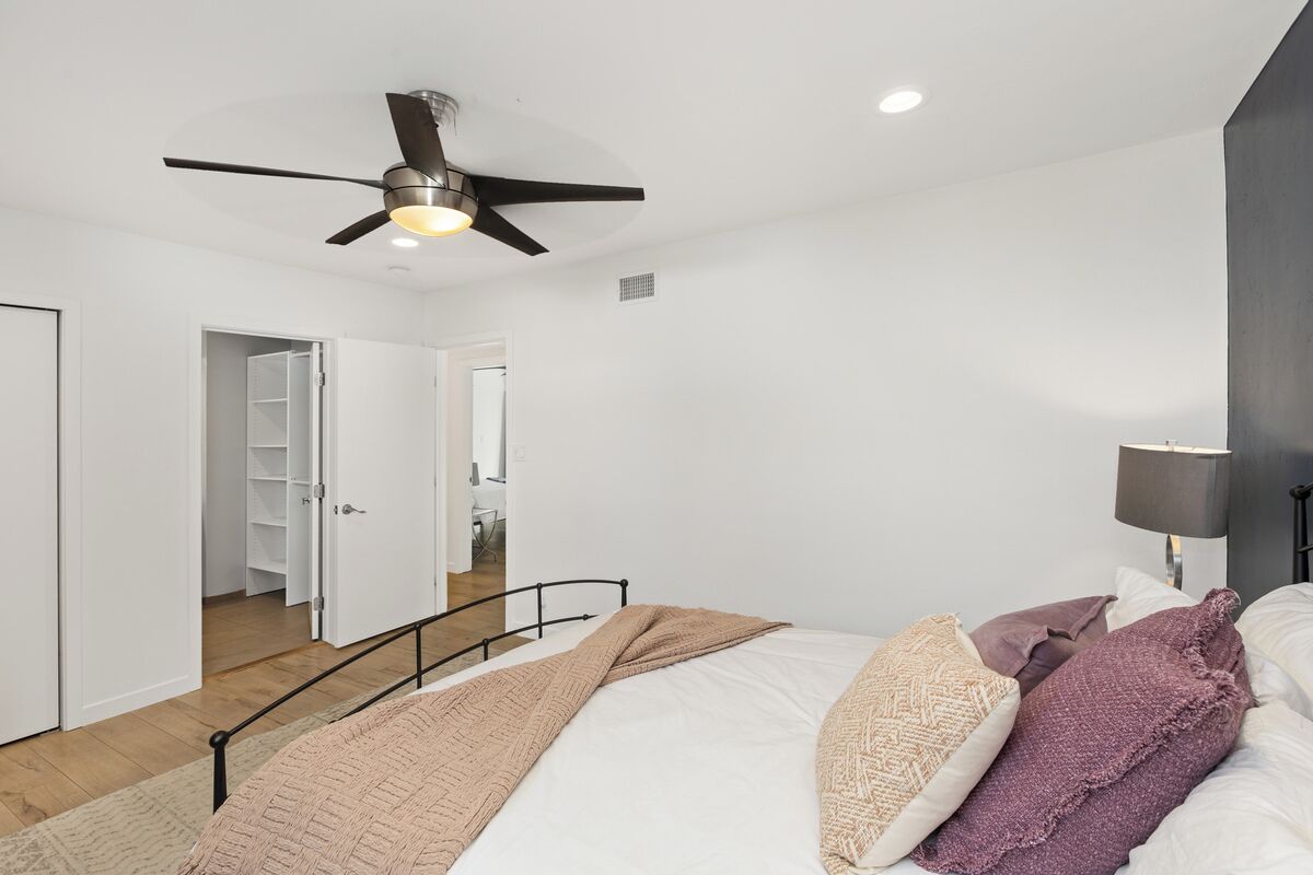 Une chambre à coucher comprenant un lit, un ventilateur de plafond, une lampe de chevet et une armoire.