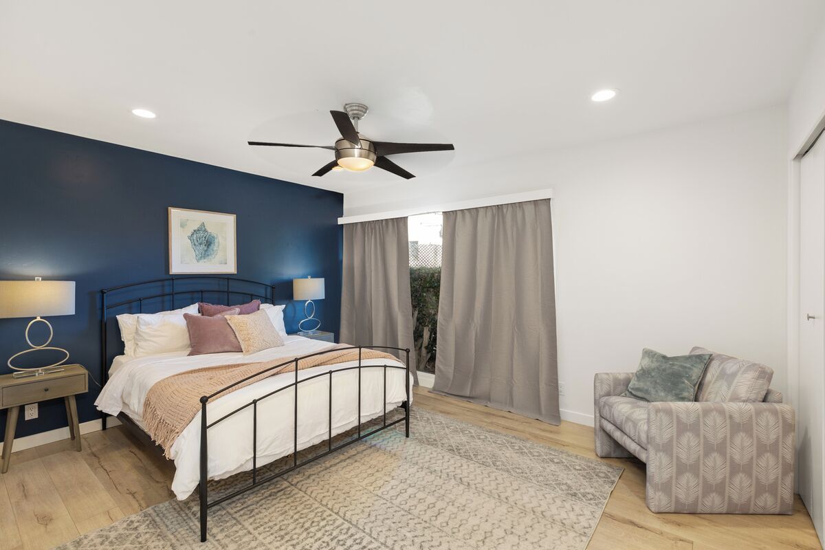 A bedroom with a bed, bedside tables, a ceiling fan, and a window with curtains.