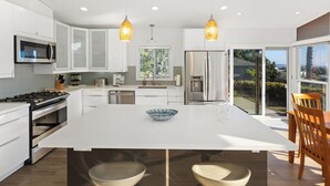 A modern kitchen with white cabinetry, a central island, and pendant lighting. - Newly Remodeled with VIEWS of Downtown Ocean and Bay! (San Diego)