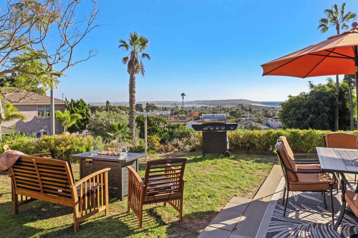 An outdoor patio area with a grill, wooden furniture, and a view of a residential neighborhood.