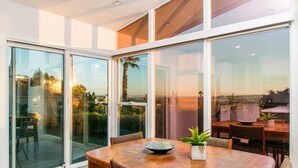 A modern dining area with a wooden table and chairs, large glass sliding doors, and a view of the outdoors. - Newly Remodeled with VIEWS of Downtown Ocean and Bay! (San Diego)