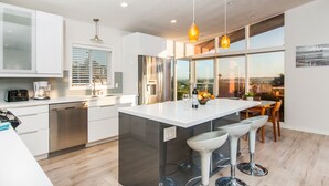 A modern kitchen with a central island, stainless steel appliances, and a large window offering a view. - Newly Remodeled with VIEWS of Downtown Ocean and Bay! (San Diego)