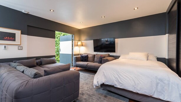 A modern bedroom with a large bed, two sofas, a TV, and a window.