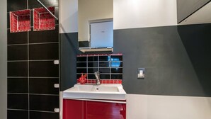 A modern kitchen with a white sink, red cabinets, and black and white tiled walls.