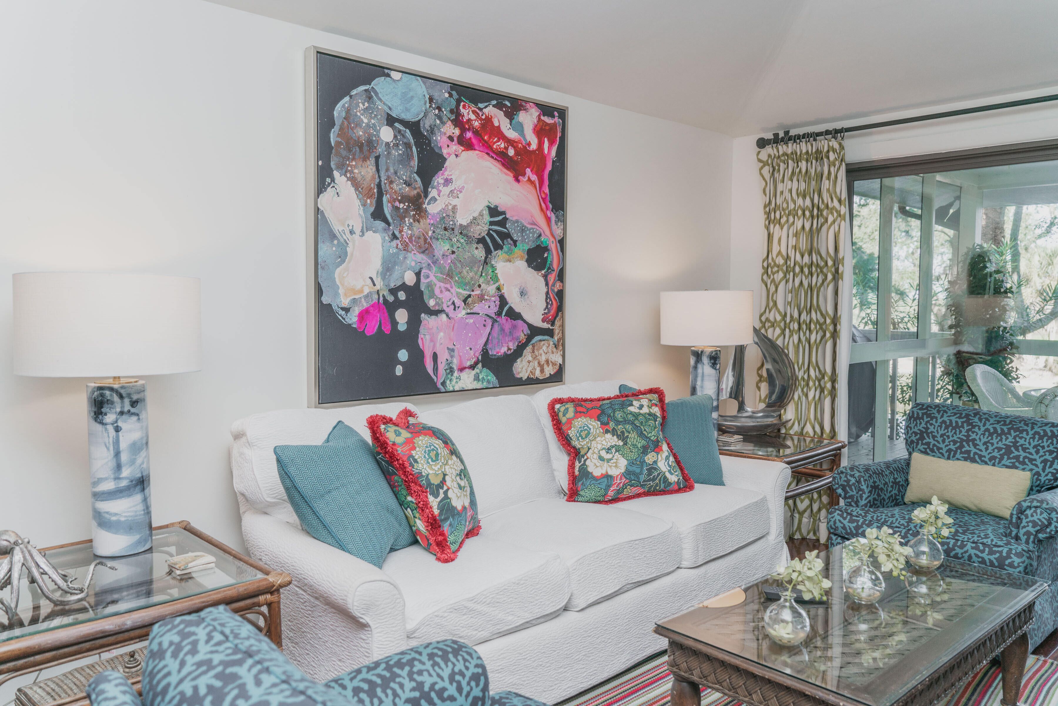 Un salon moderne avec un canapé blanc, des coussins à motifs, une table basse en verre et un grand tableau abstrait accroché au mur.