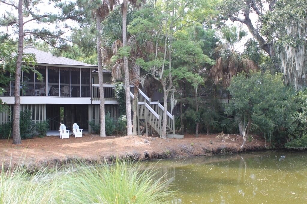 A lakeside cabin with a covered deck, outdoor seating, and a staircase leading to the main building.