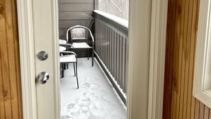 A door leading to a covered porch with a metal railing and two chairs.