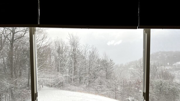 A window with a view of a snow-covered landscape, including trees and a hill.