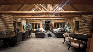 A log cabin interior with a fireplace, two sofas, a dining table, and Christmas trees. - A large, newly remodeled 7,000 sq ft cabin, new hot tub, minutes from Deadwood! (Lead)