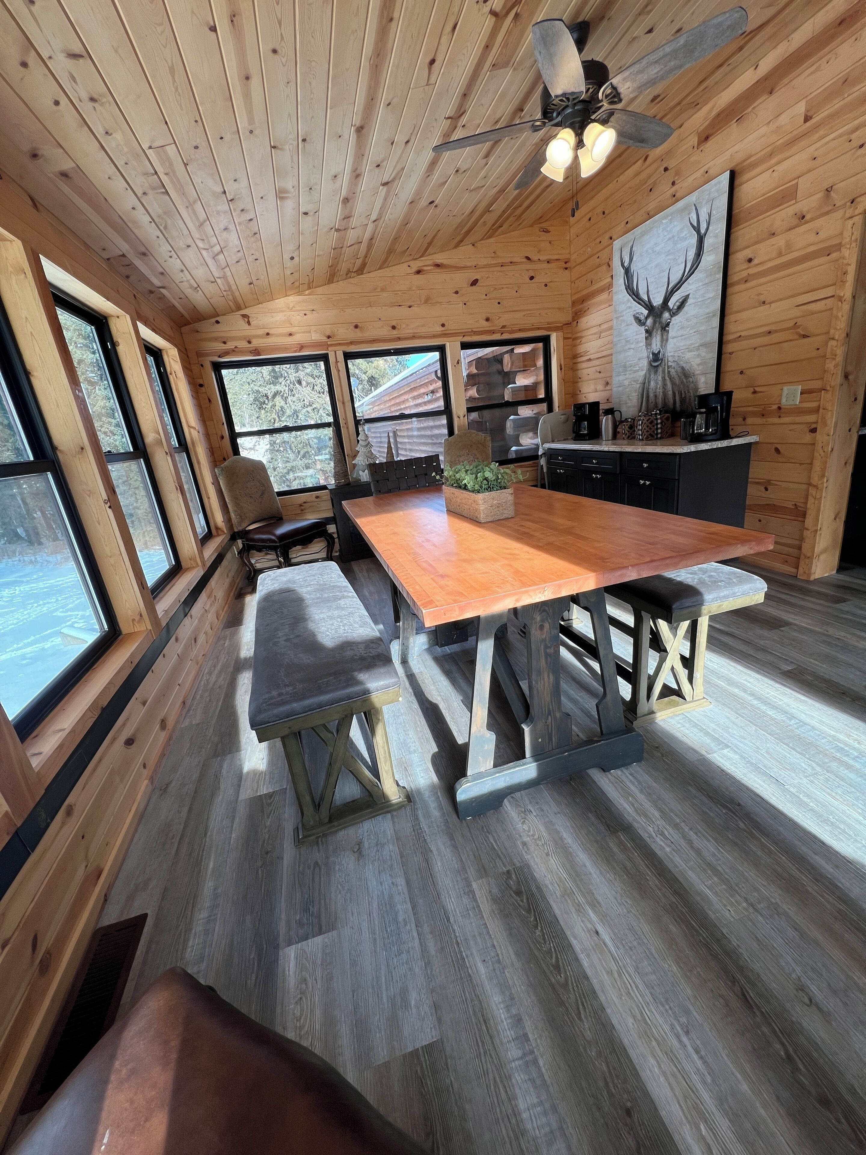A wooden interior with a large dining table, chairs, and a ceiling fan.