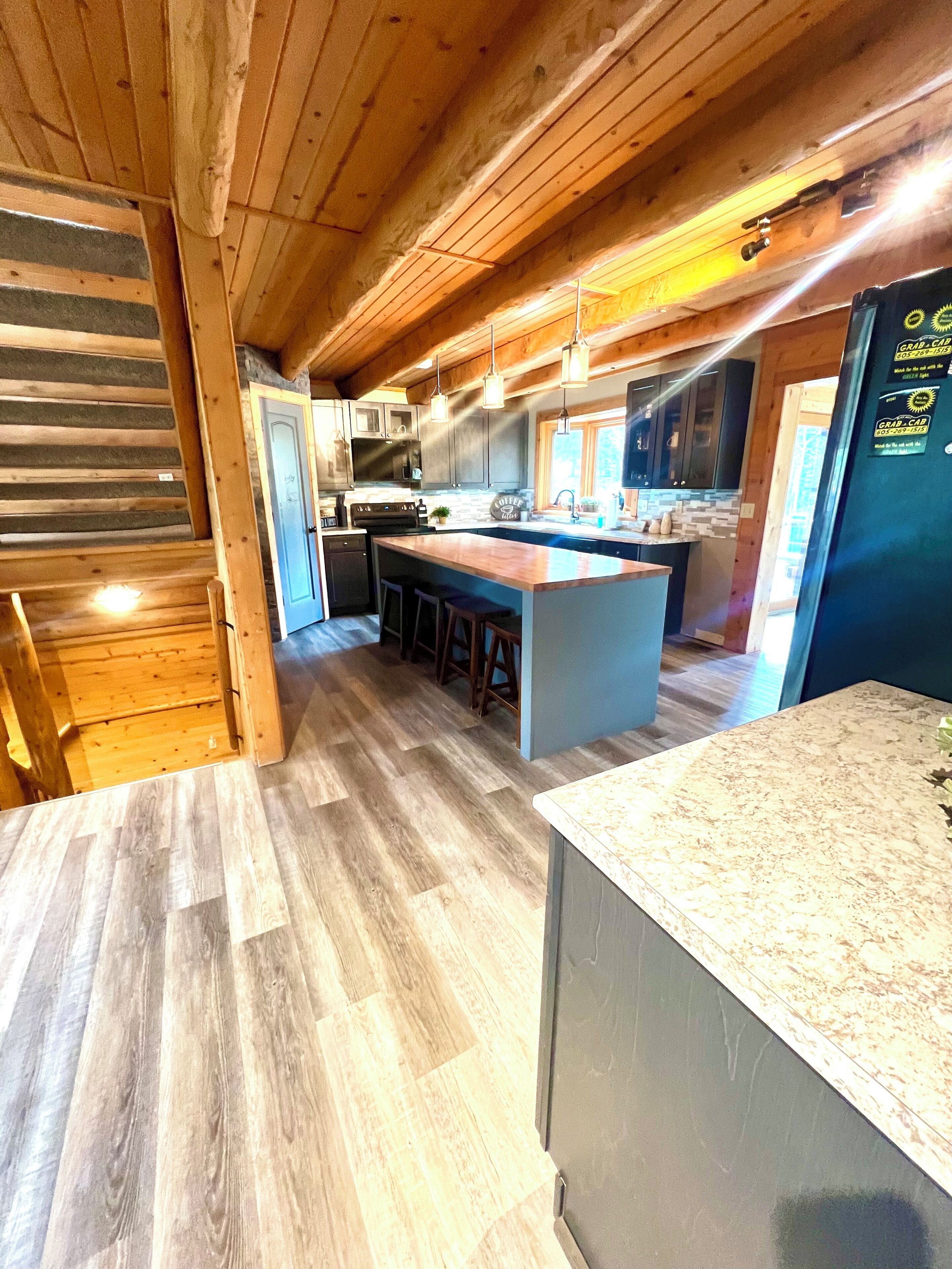 Une cuisine moderne avec des poutres en bois, un îlot central, des tabourets de bar et un réfrigérateur décoré d’aimants.