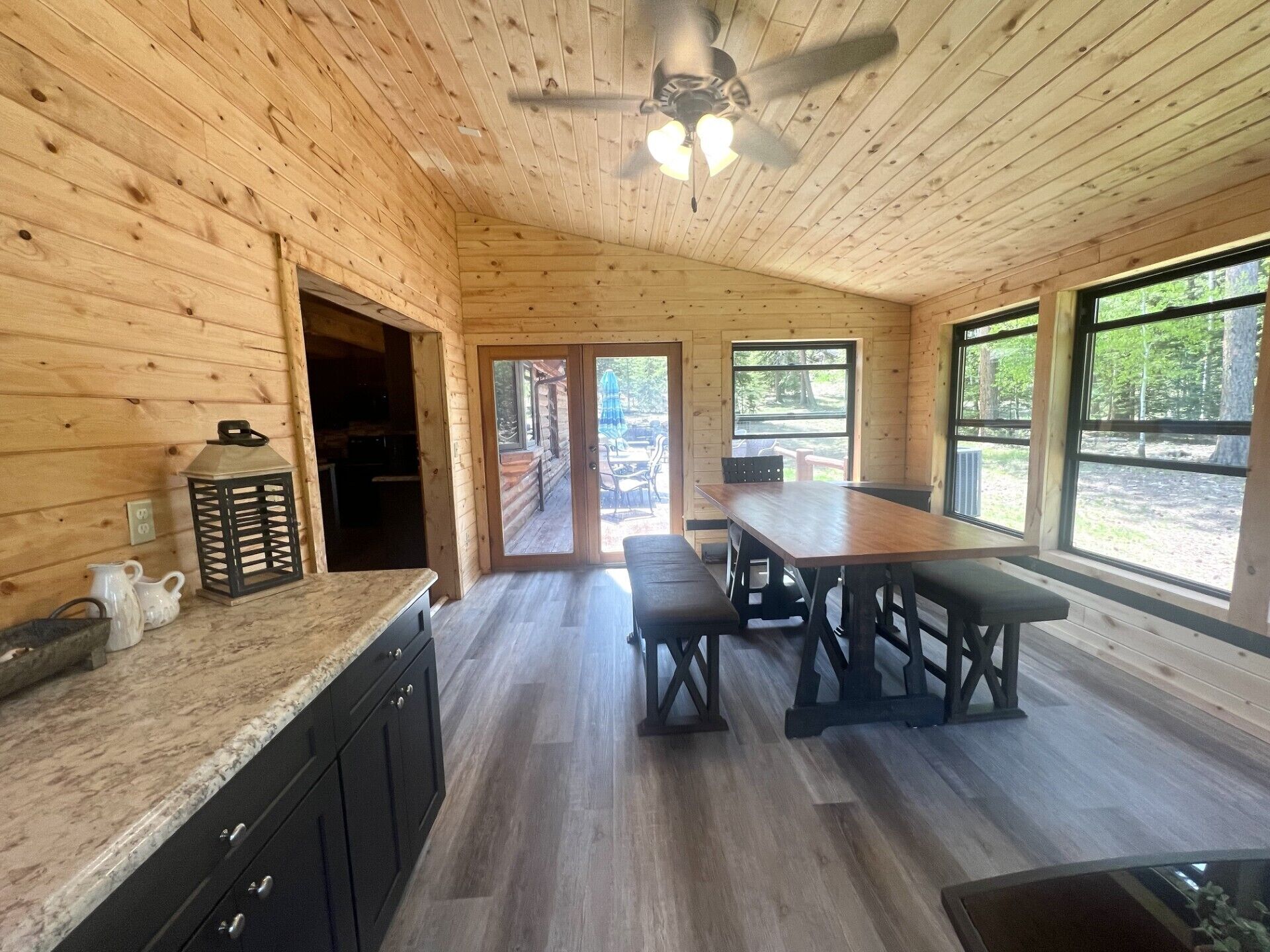 A wooden cabin interior with a kitchen, dining area, and large windows.