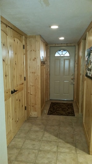 A hallway with wooden paneling, a white door with a window, and a tiled floor.