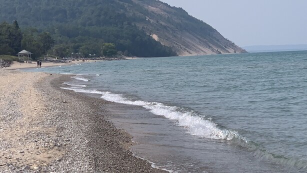 A pebbly beach with a gazebo and a hill in the background.